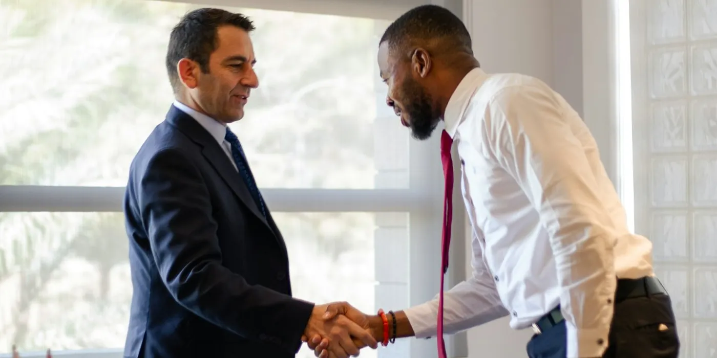 Two professionals shaking hands by a bright window (illustrative)