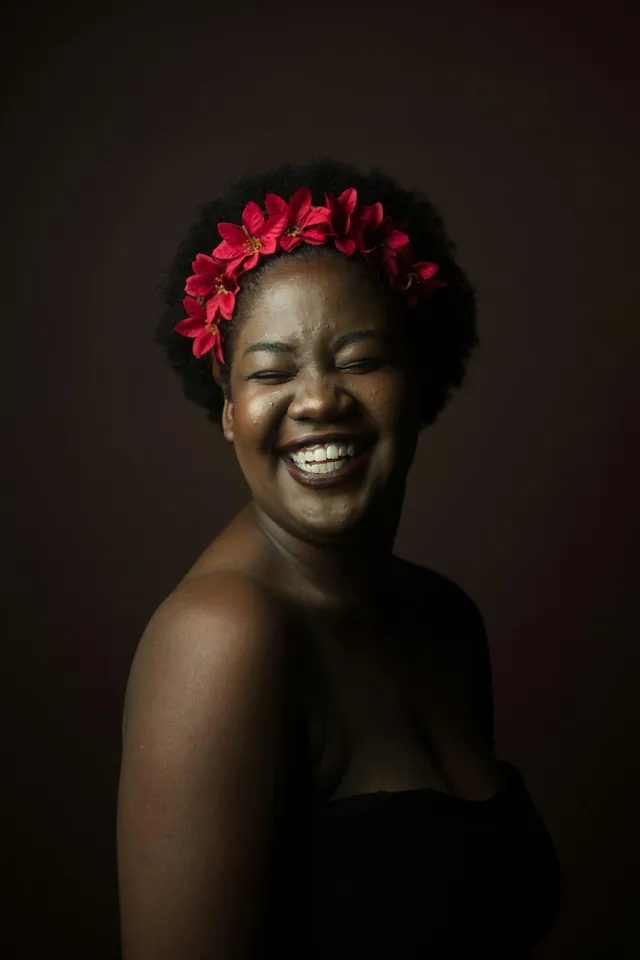 A laughing woman with a red flower crown in a dark studio portrait (illustrative)