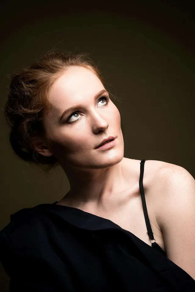 A woman in black looking upward in warm studio light (illustrative)